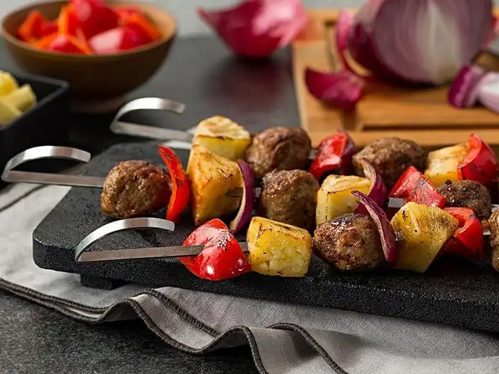 Teriyaki-style chicken meatball skewers with pineapple, red bell pepper, and red onion arranged on a dark slate serving board